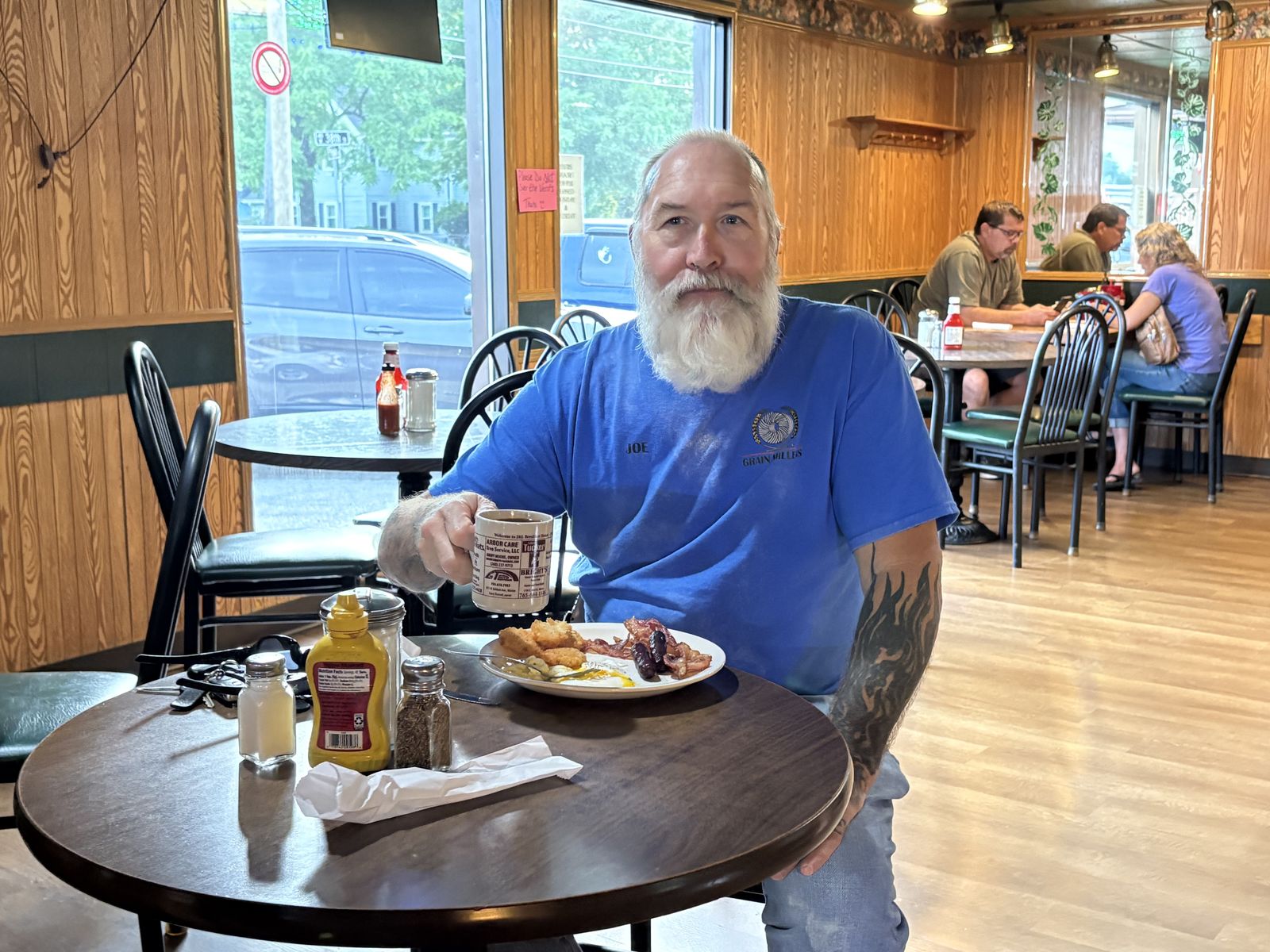 A regular raising his coffee mug over a plate of eggs, bacon and hash browns